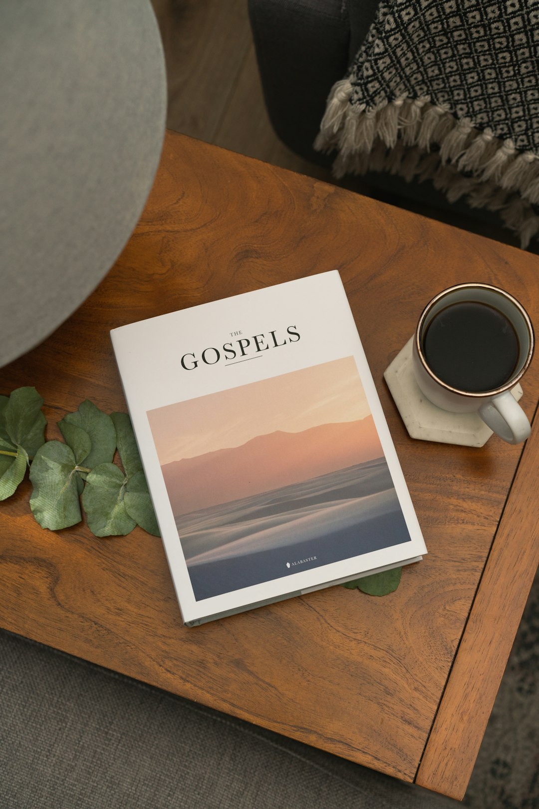 Alabaster Gospels Hardcover Bible book on wooden table with coffee and plant
